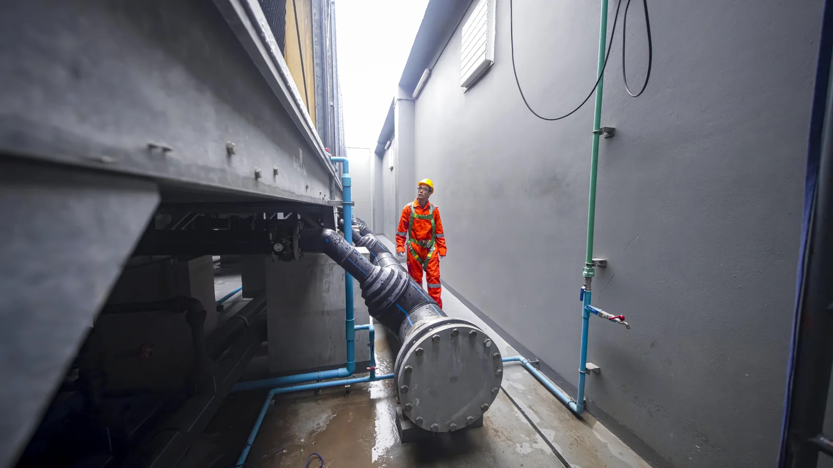 Worker inspecting industrial pipes in a narrow access area