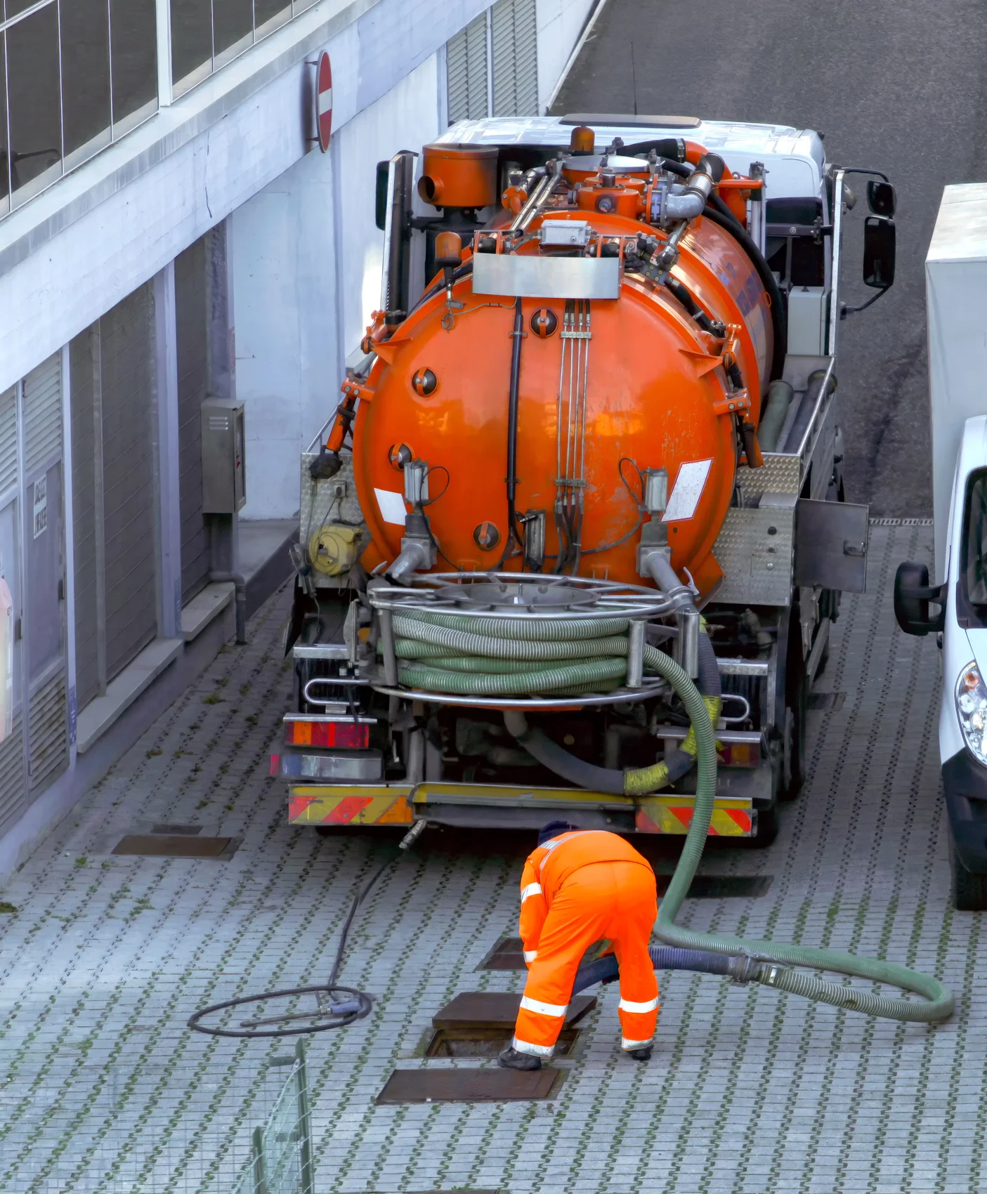 Worker lowering a sewer cleaning hose into a sewer pit to clear buildup