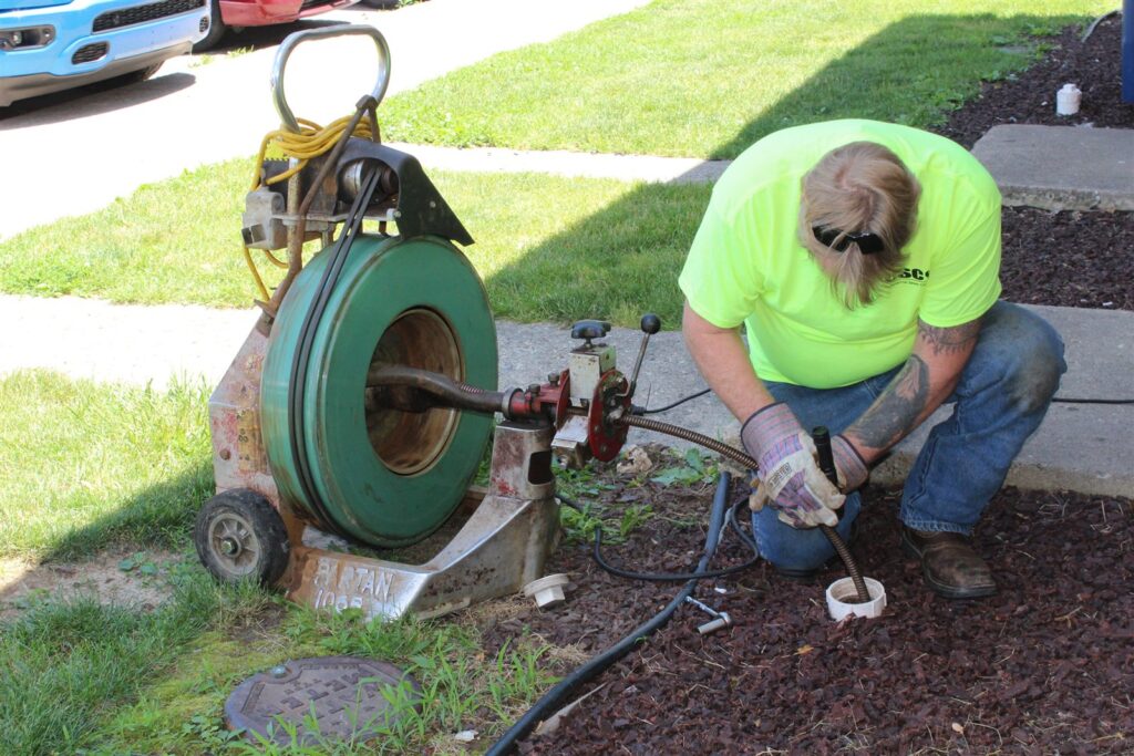 CSC technician snaking a drain with a drum cable machine at an outdoor cleanout